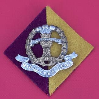 The Middlesex Regiment - Bi Metal Cap Badge With Cloth Backing.